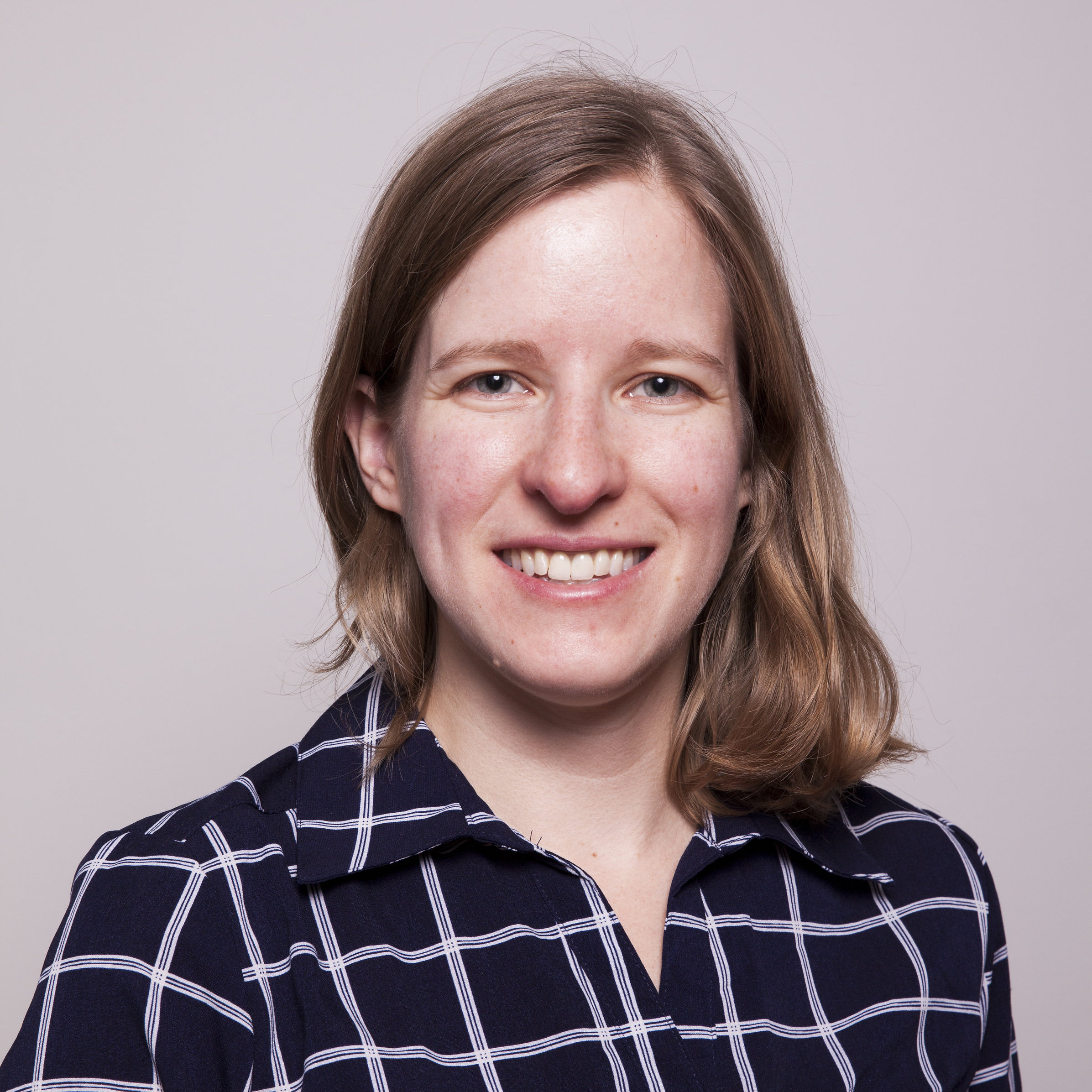 Kelly Bowker, Caucasian female smiling, wearing a navy blue with white window pane grid button down shirt
